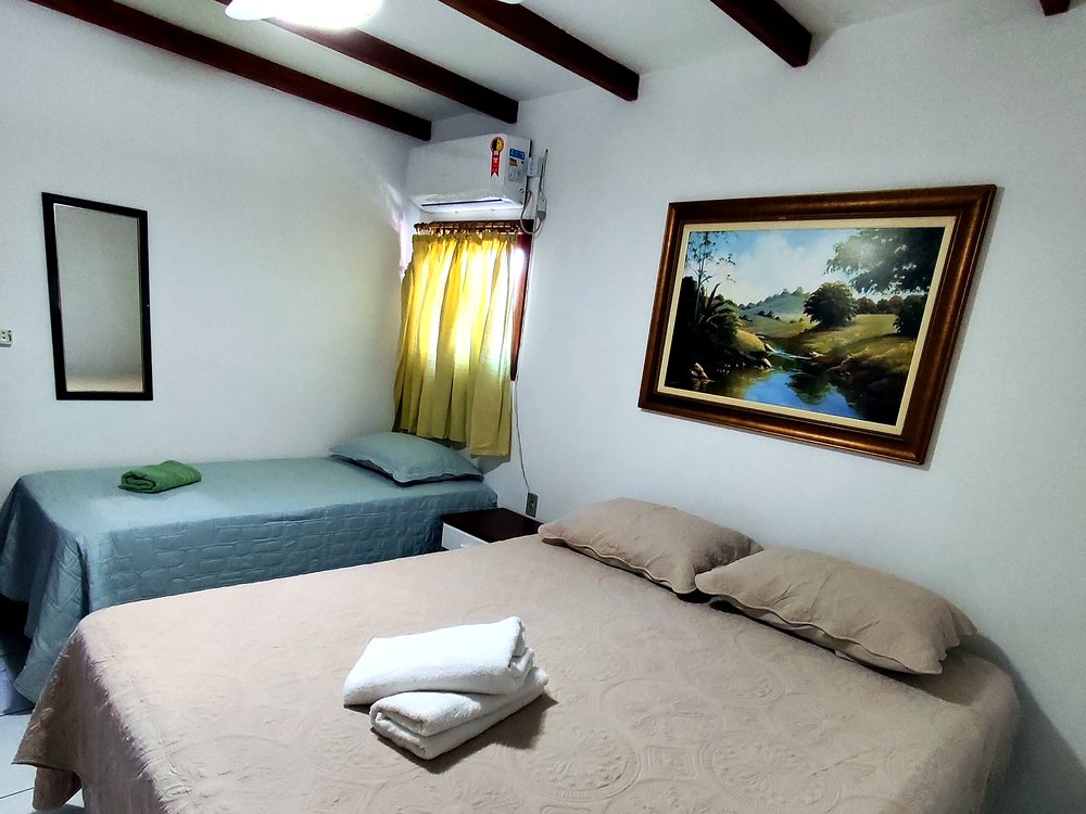 Quarto do térreo do Loft da Pousada Capricórnio, com cama de casal, cama de solteiro e teto com vigas de madeira aparentes