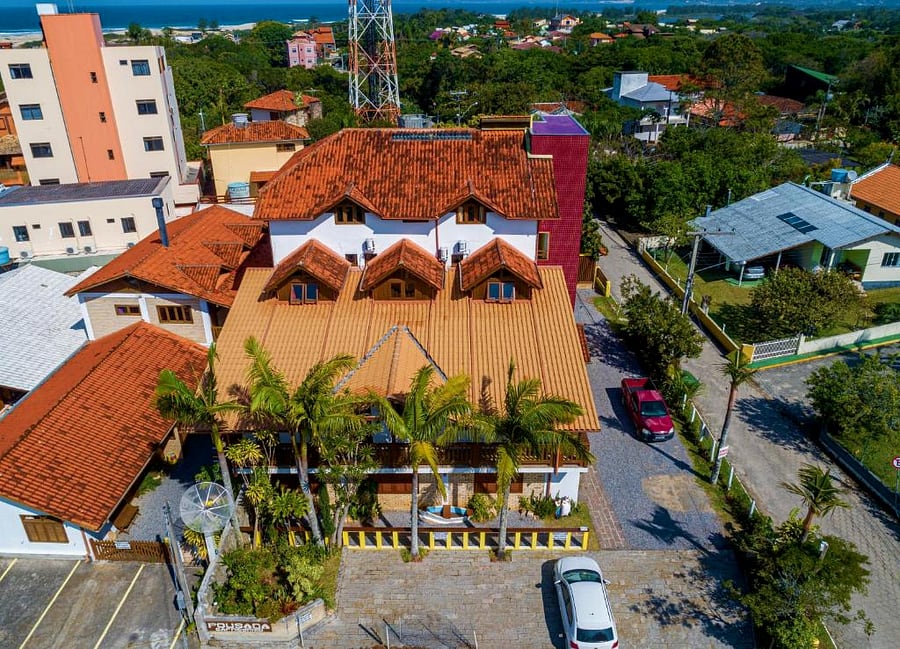 Vista aérea da Pousada Capricórnio, com o telhado do prédio principal, jardim e o mar da Guarda do Embaú ao fundo