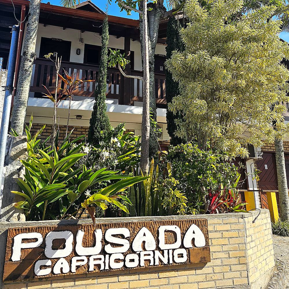 Entrada da Pousada Capricórnio, com jardim tropical e fachada avistada por trás das palmeiras